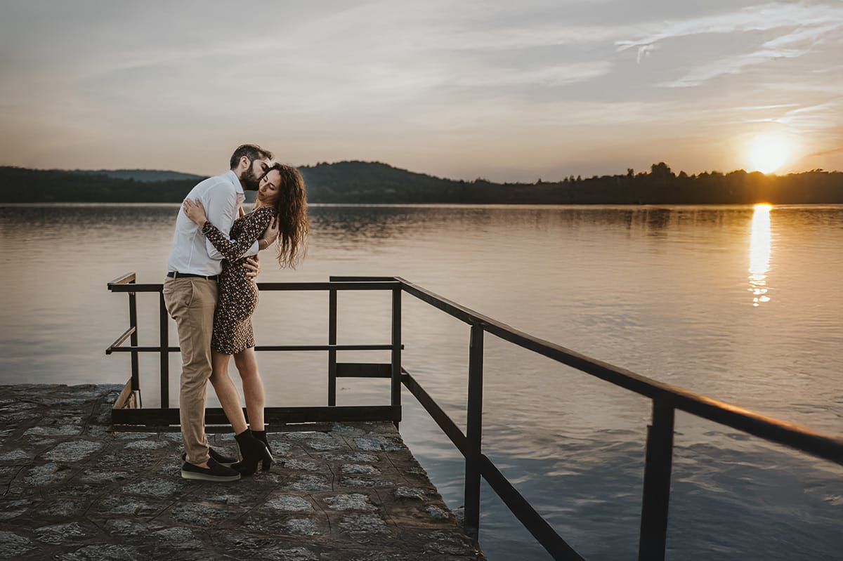 Pre-wedding al Lago di Viverone di Ilaria e Luca. Ilaria e Luca uno di fronte all'altra con sulla sfondo il lago e il sole che tramonta.