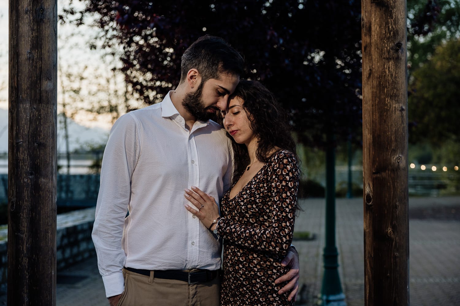 Pre-wedding al Lago di Viverone di Ilaria e Luca. Sposi abbracciati sul pontile di legno decorato da una fila di lampadine. Sullo sfondo un bellissimo tramonto.