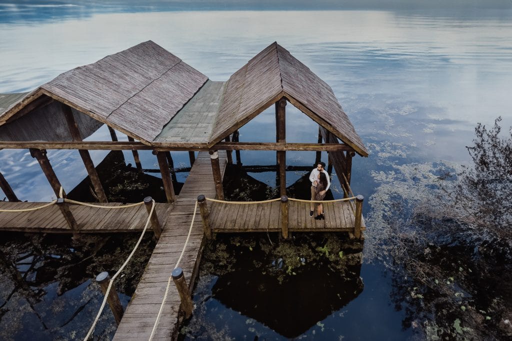Ilaria and Luca's enchanting pre-wedding shoot at Lake Viverone. Aerial drone capture of the couple on the pier against the backdrop of prehistoric pile dwellings