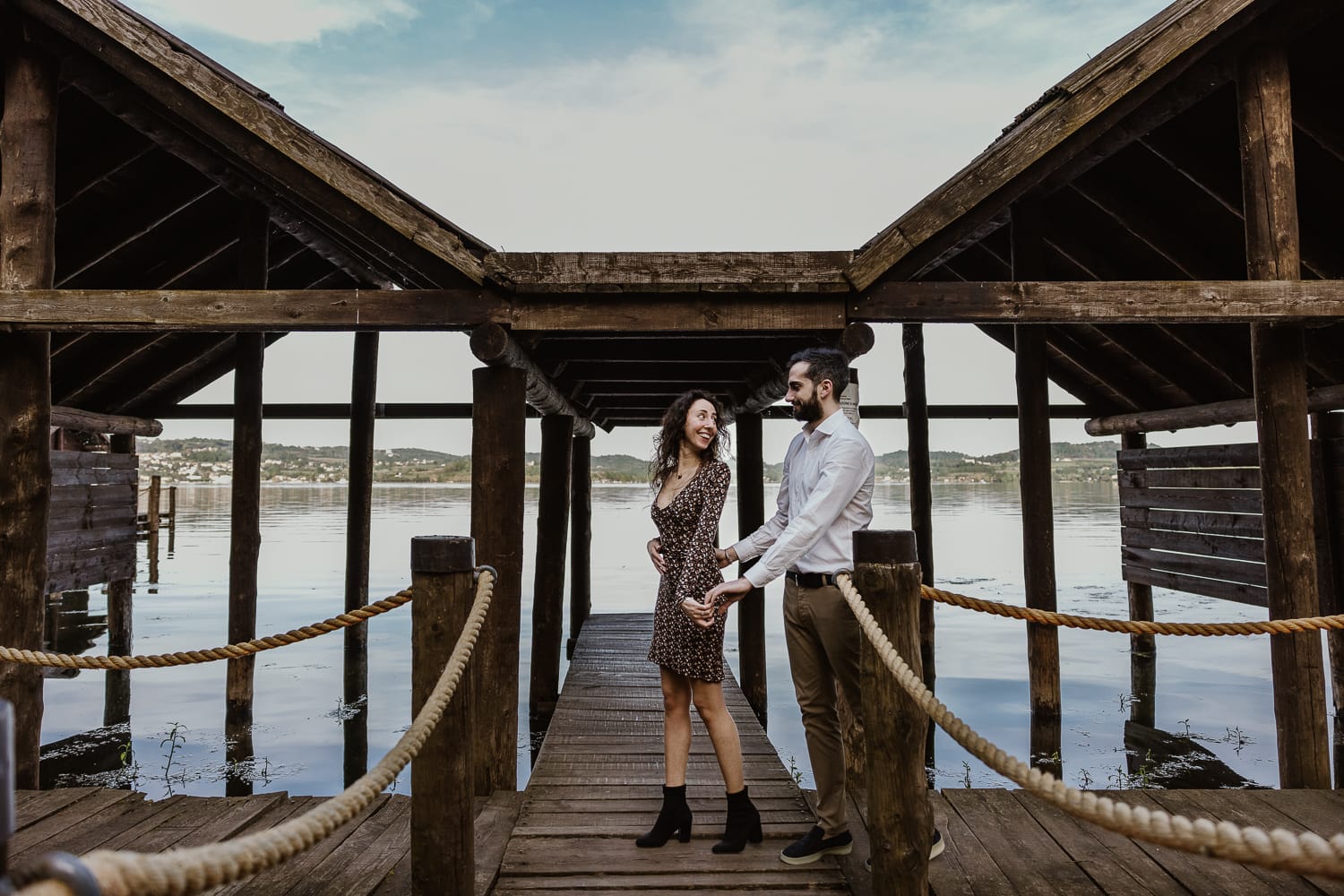 Pre-wedding al Lago di Viverone di Ilaria e Luca. Ilaria tira Luca camminando sul pontile delle palafitte.