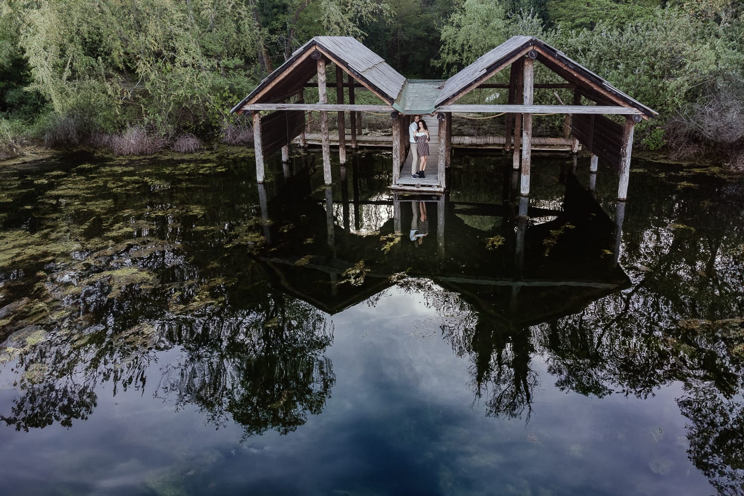 Pre-wedding al Lago di Viverone di Ilaria e Luca. Foto aerea dal drone della coppia tra le palafitte. La coppia è riflessa nel lago.