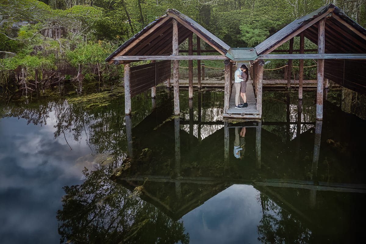 Pre-wedding al Lago di Viverone di Ilaria e Luca. Foto aerea dal drone della coppia tra le palafitte. La coppia è riflessa nel lago.
