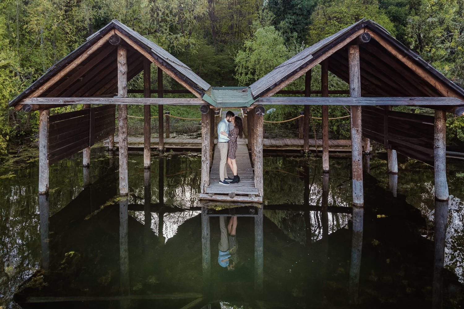 Pre-wedding al Lago di Viverone di Ilaria e Luca. Foto aerea dal drone della coppia tra le palafitte. La coppia è riflessa nel lago.