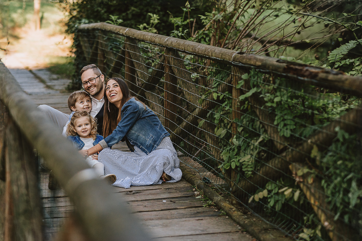Fotografia di famiglia a Chieri, nel Giardino del Tessile. La famiglia è seduta sul ponte di legno sopra il Rio Tepice. La famiglia guarda in alto verso il drone.