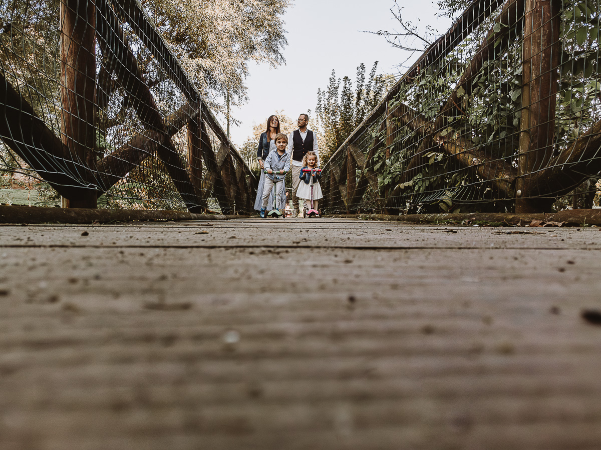 Fotografia di famiglia a Chieri, nel Giardino del Tessile. La famiglia è sul ponte di legno sopra il Rio Tepice. I bambini sono sui monopattini.