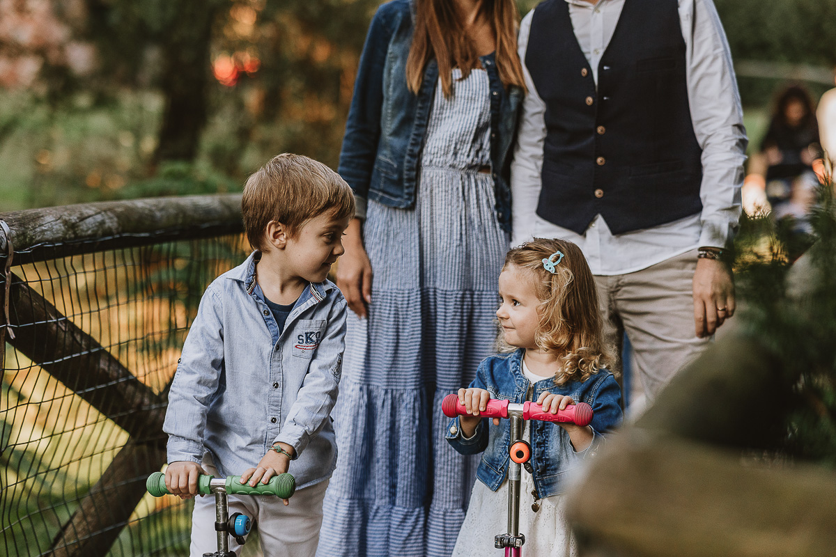 Fotografia di famiglia a Chieri, nel Giardino del Tessile. La famiglia è sul ponte di legno sopra il Rio Tepice. I bambini sono sui monopattini e si guardano.