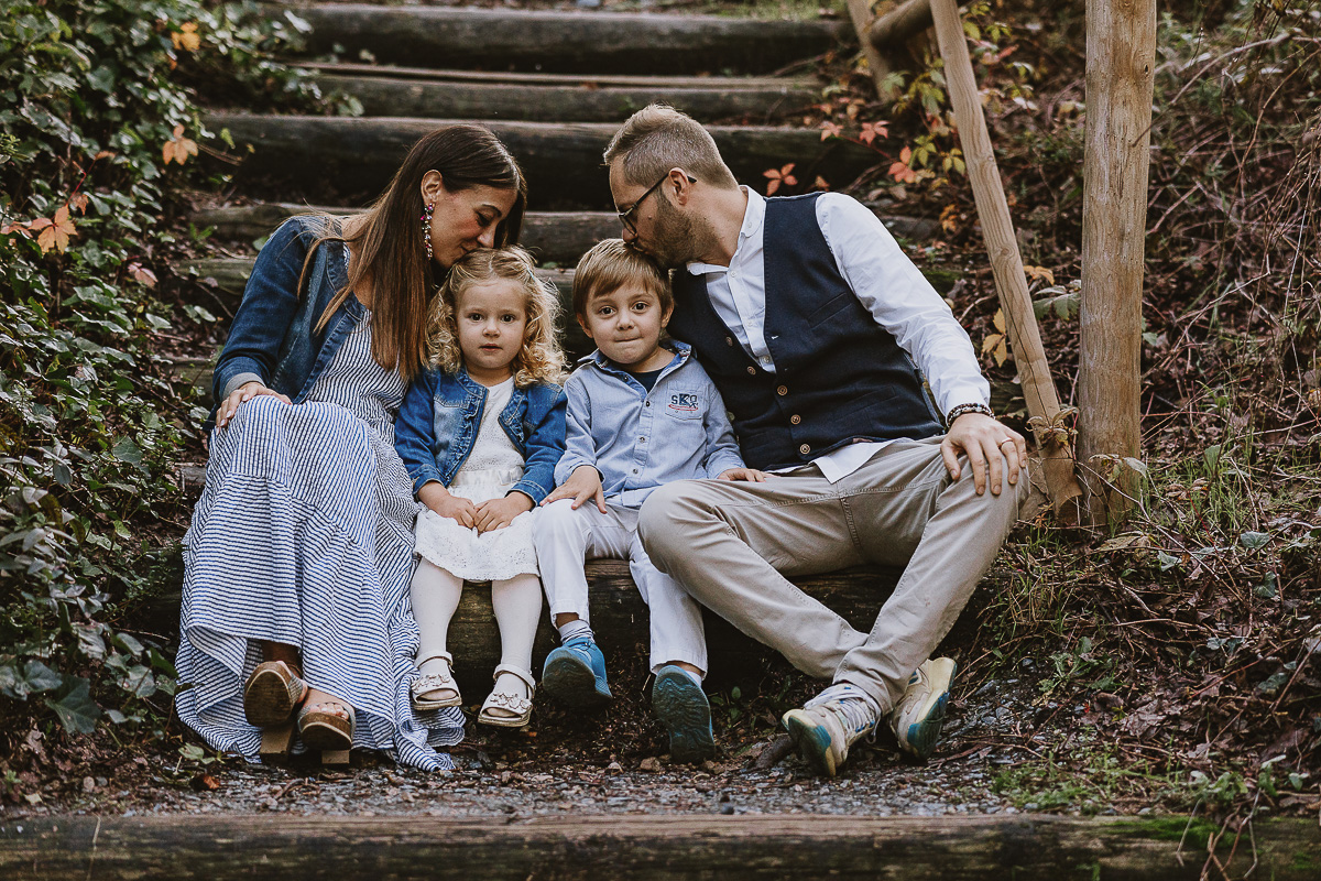 Fotografia di famiglia a Chieri, nel Giardino del Tessile. La famiglia è seduta al fondo di una scalinata rustica di tronchi.