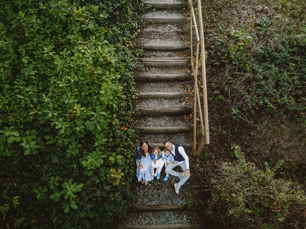 Fotografia di famiglia a Chieri, nel Giardino del Tessile. La famiglia è seduta al fondo di una scalinata rustica di tronchi.