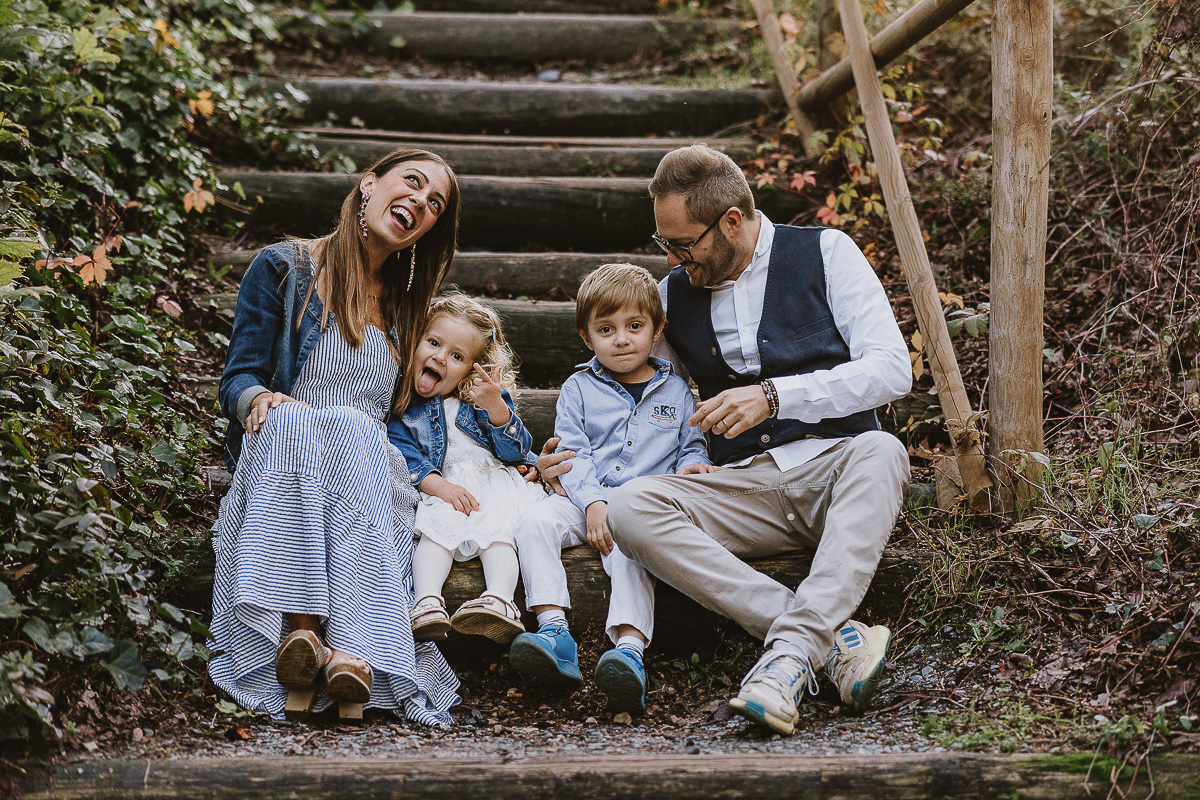 Fotografia di famiglia a Chieri, nel Giardino del Tessile. La famiglia è seduta al fondo di una scalinata rustica di tronchi.