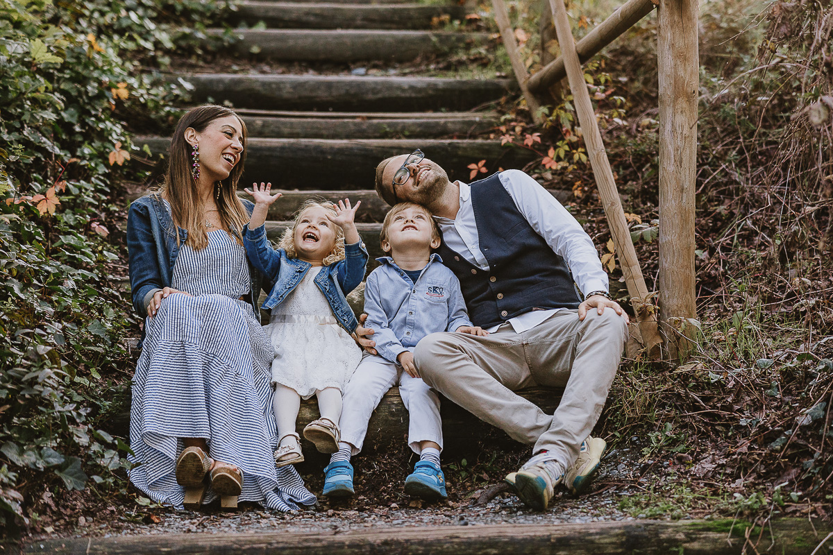 Fotografia di famiglia a Chieri, nel Giardino del Tessile. La famiglia è seduta al fondo di una scalinata rustica di tronchi.