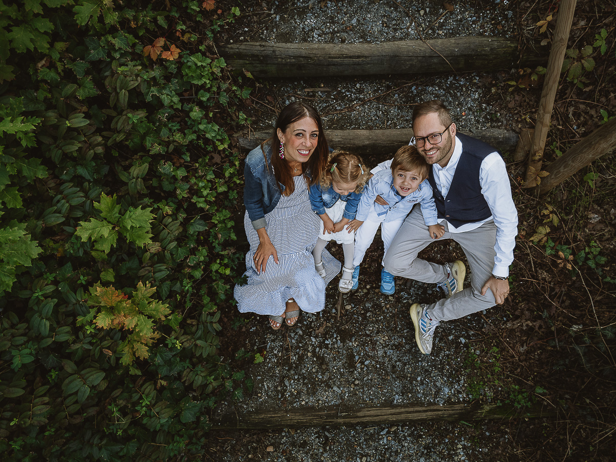 Fotografia di famiglia a Chieri, nel Giardino del Tessile. La famiglia è seduta al fondo di una scalinata rustica di tronchi.