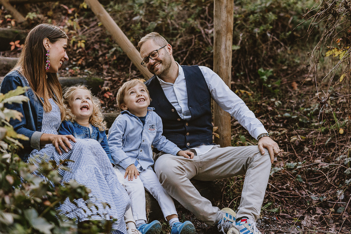 Fotografia di famiglia a Chieri, nel Giardino del Tessile. La famiglia è seduta al fondo di una scalinata rustica di tronchi.