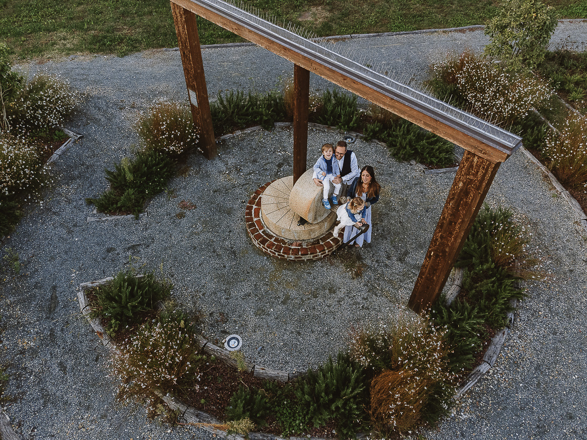 Fotografia di famiglia a Chieri, nel Giardino del Tessile. Tutta la famiglia vicino alla Macina. I bambini sono seduti sulla Macina. Foto aerea dal drone
