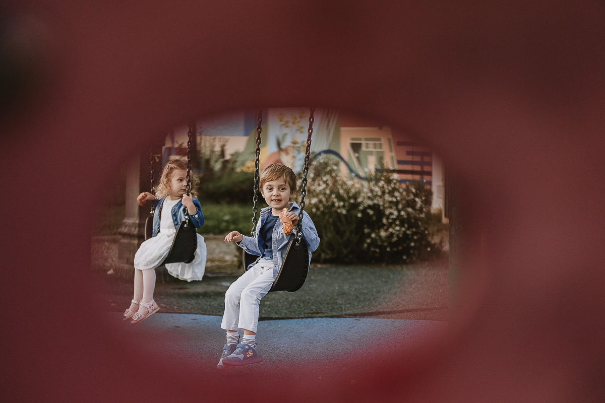 Fotografia di famiglia a Chieri, nel Giardino del Tessile. Camilla ed Edo sull'altalena ripresi attraverso un foro dello scivolo.