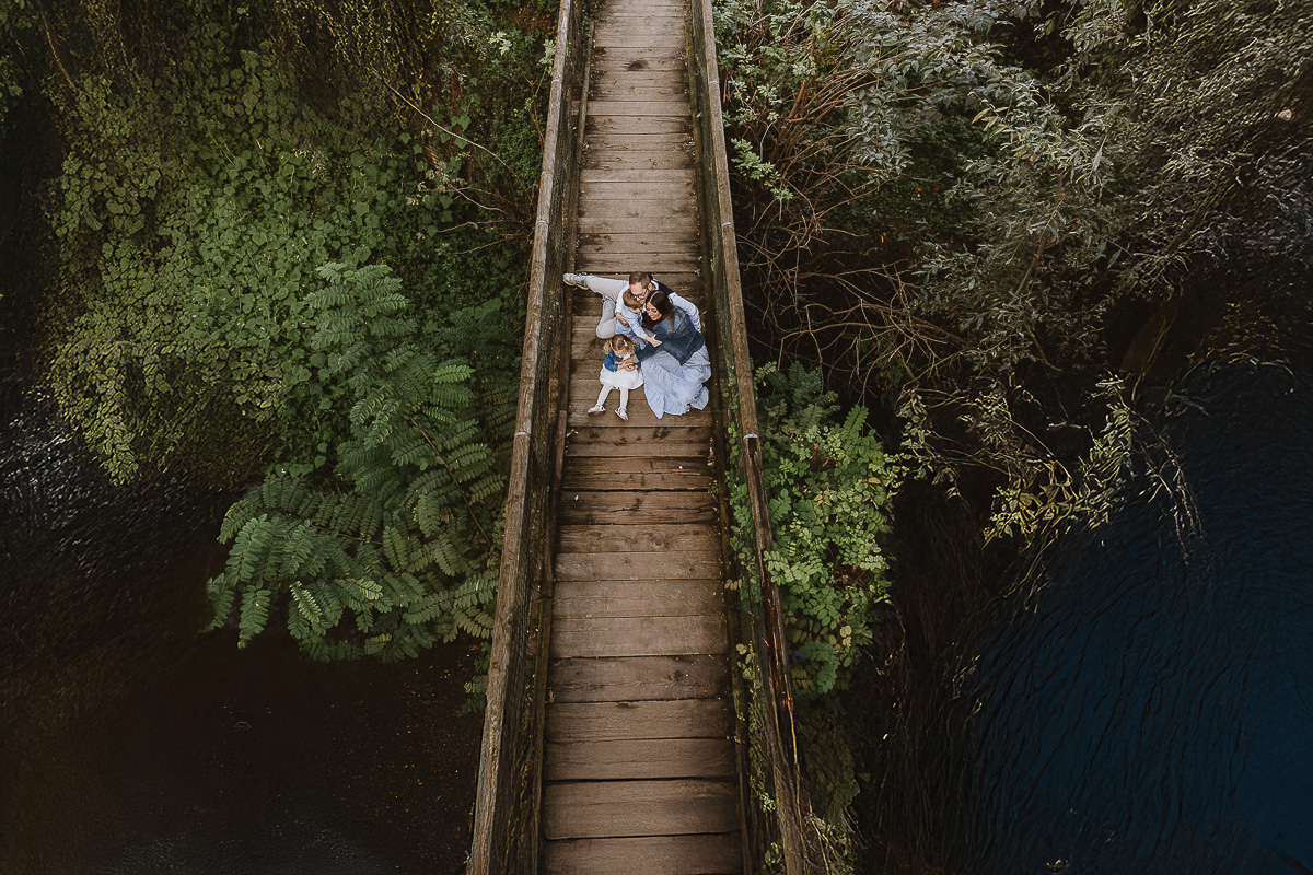 Fotografia di famiglia a Chieri, nel Giardino del Tessile. La famiglia è seduta sul ponte di legno sopra il Rio Tepice. Foto aerea dal drone.