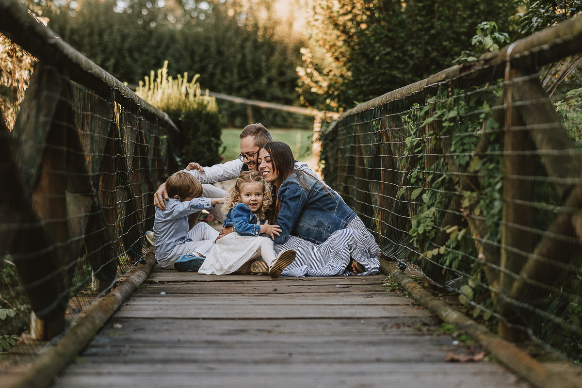 Fotografia di famiglia a Chieri, nel Giardino del Tessile. La famiglia è seduta sul ponte di legno sopra il Rio Tepice. Si abbracciano