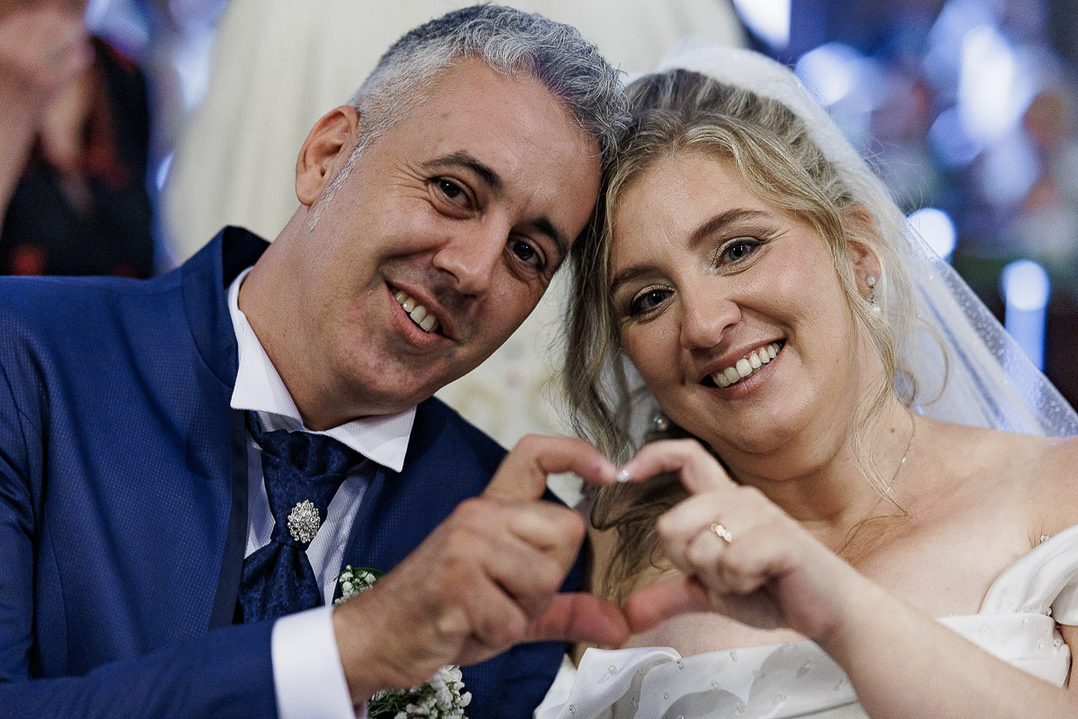 Fotografo Matrimonio in Piemonte. Cerimonia nella chiesa di San Giovanni Battista di Moriondo Torinese. Sposi fanno un cuore con le dita.