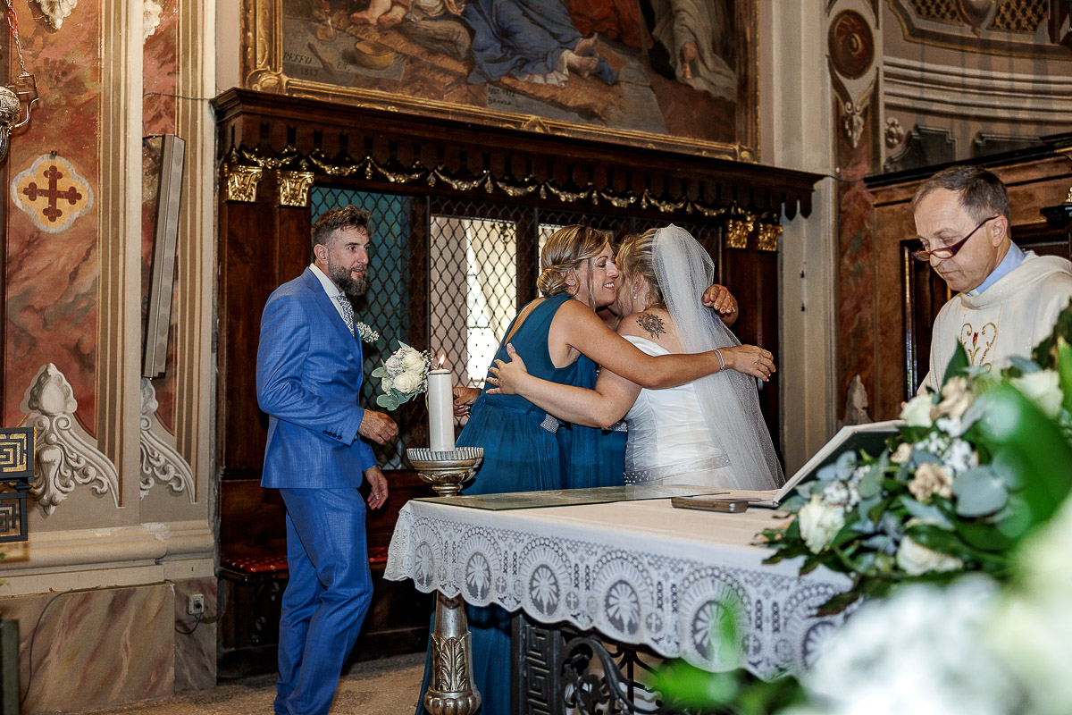 Fotografo Matrimonio in Piemonte. Cerimonia nella chiesa di San Giovanni Battista di Moriondo Torinese. testimoni abbracciano la sposa.