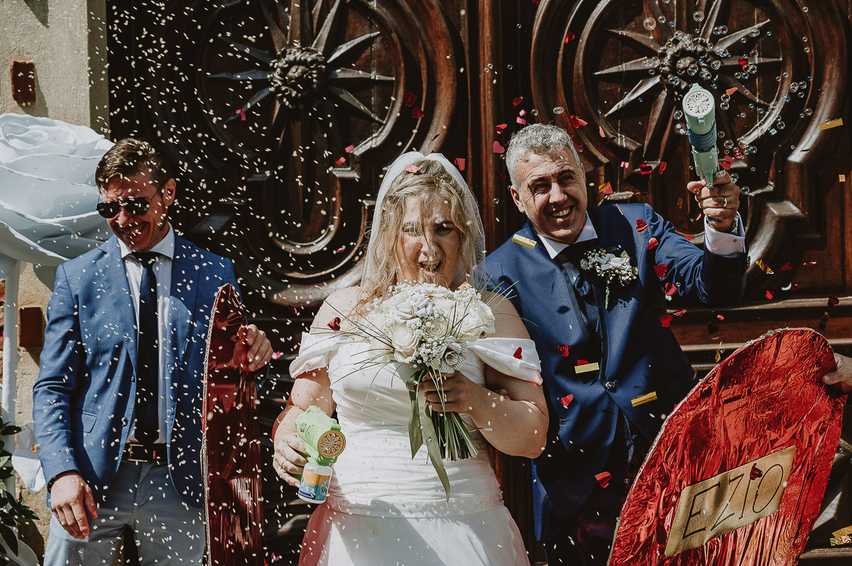Fotografo Matrimonio in Piemonte. Cerimonia nella chiesa di San Giovanni Battista di Moriondo Torinese. Uscita degli sposi. Gli amici mettono un grande cuore davanti a loro. Gli sposi sparano le bolle con due fucili sparabolle.