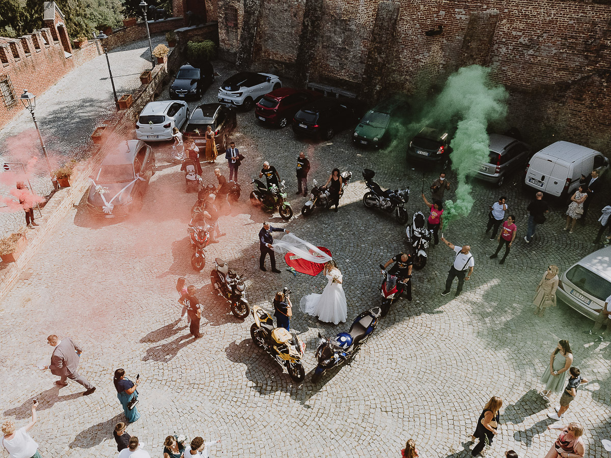 Fotografo Matrimonio in Piemonte. Cerimonia nella chiesa di San Giovanni Battista di Moriondo Torinese. All'uscita gli amici motociclisti hanno creato un cuore con le moto e acceso dei fumi colorati rossi e verdi. lo sposo tira il velo alla sposa. Foto aerea dal drone.