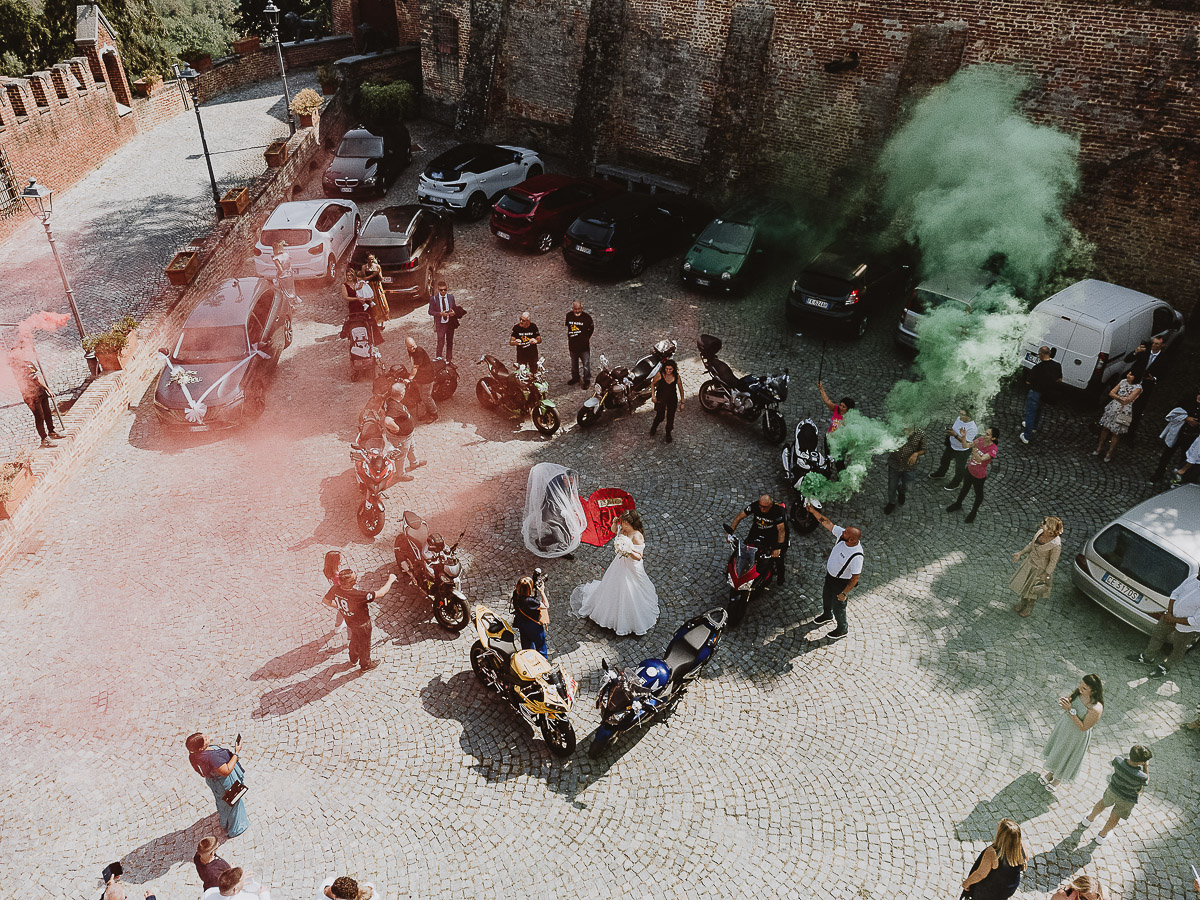 Fotografo Matrimonio in Piemonte. Cerimonia nella chiesa di San Giovanni Battista di Moriondo Torinese. All'uscita gli amici motociclisti hanno creato un cuore con le moto e acceso dei fumi colorati rossi e verdi. Lo sposo tira il velo alla sposa.