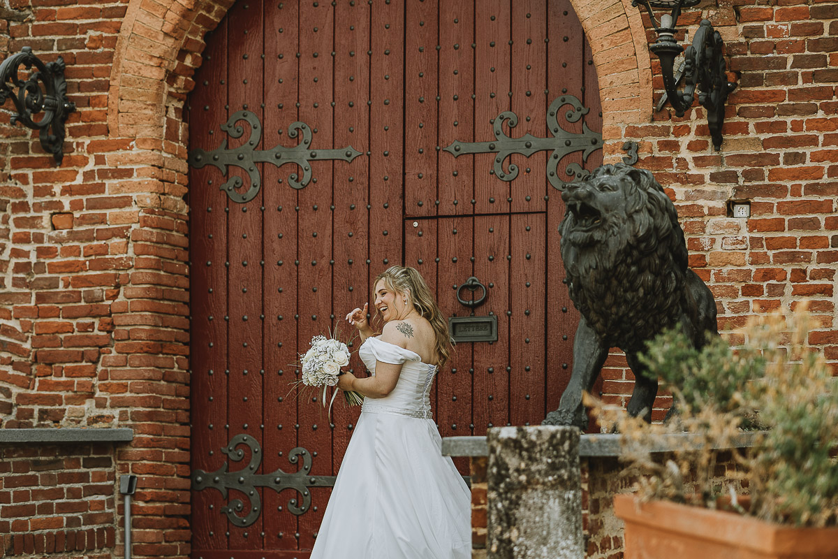 Fotografo Matrimonio in Piemonte. Ritratti di coppia degli sposi davanti al castello di Moriondo Torinese. Sposa davanti al portrone del castello ruggisce come i leoni di pietra