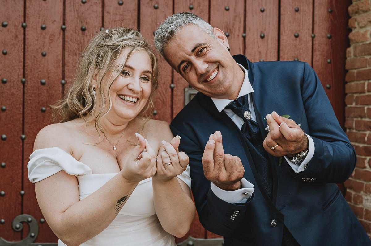 Fotografo Matrimonio in Piemonte. Ritratti di coppia degli sposi davanti al castello di Moriondo Torinese. Gli sposi fanno il simbolo cinese di amore con le dita.