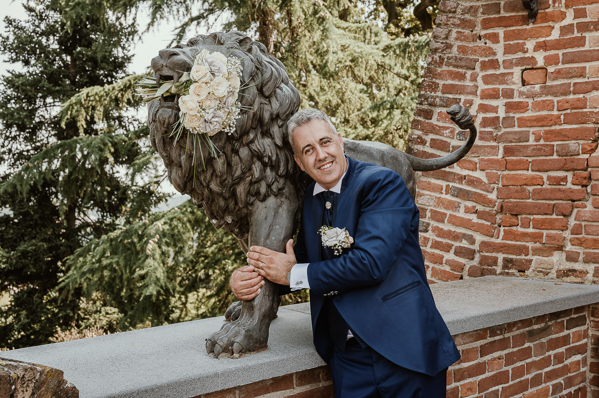 Fotografo Matrimonio in Piemonte. Ritratti di coppia degli sposi davanti al castello di Moriondo Torinese. Sposo davanti al leone di bronzo che ha in bocca il bouquet