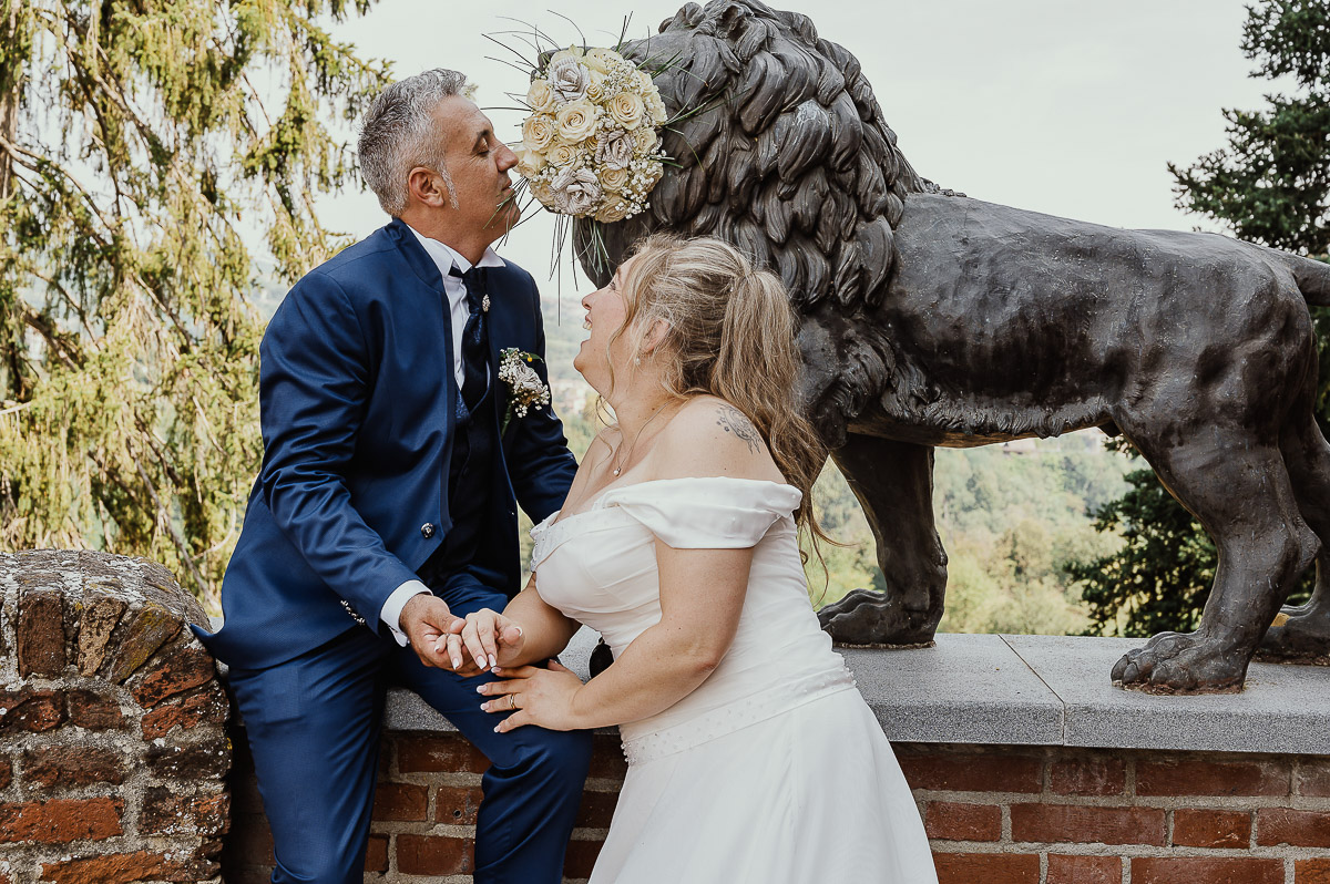 Fotografo Matrimonio in Piemonte. Ritratti di coppia degli sposi davanti al castello di Moriondo Torinese. Sposi davanti al leone di bronzo che ha in bocca il bouquet