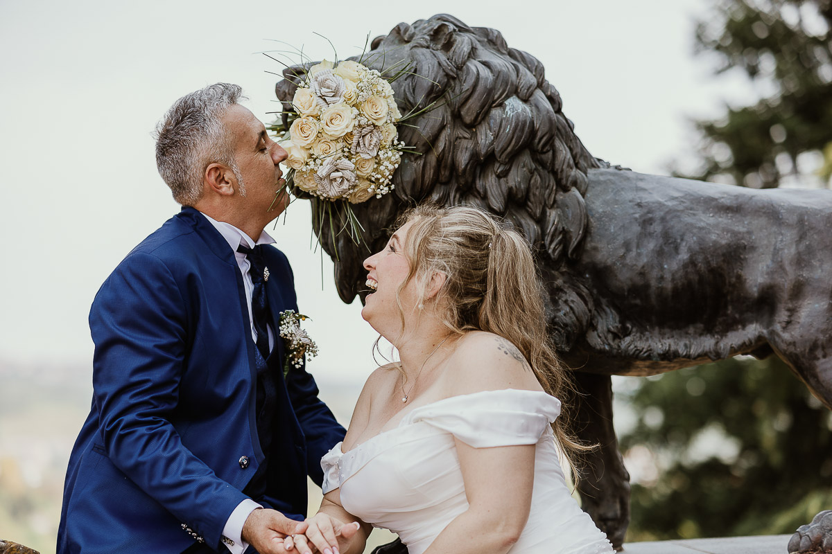 Fotografo Matrimonio in Piemonte. Ritratti di coppia degli sposi davanti al castello di Moriondo Torinese. Sposi davanti al leone di bronzo che ha in bocca il bouquet