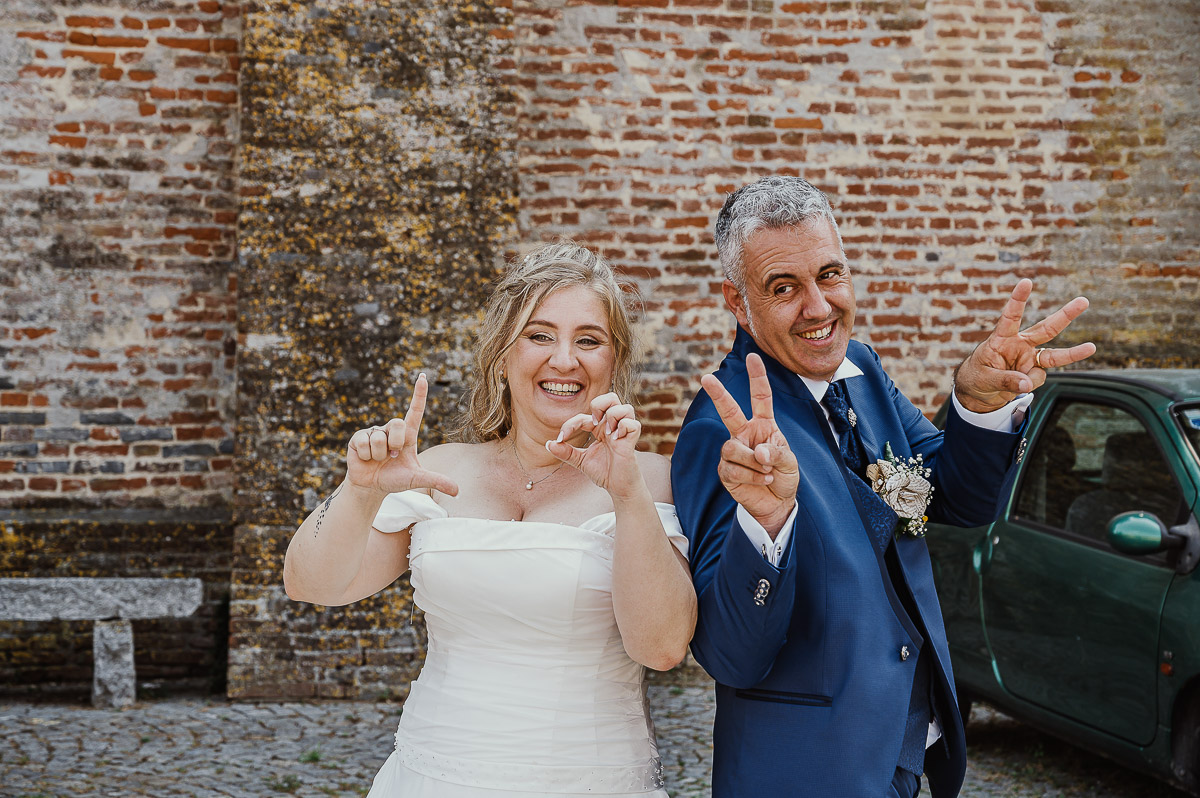 Fotografo Matrimonio in Piemonte. Ritratti di coppia degli sposi davanti al castello di Moriondo Torinese. Gli sposi scrivono la parola LOVE con le dita.