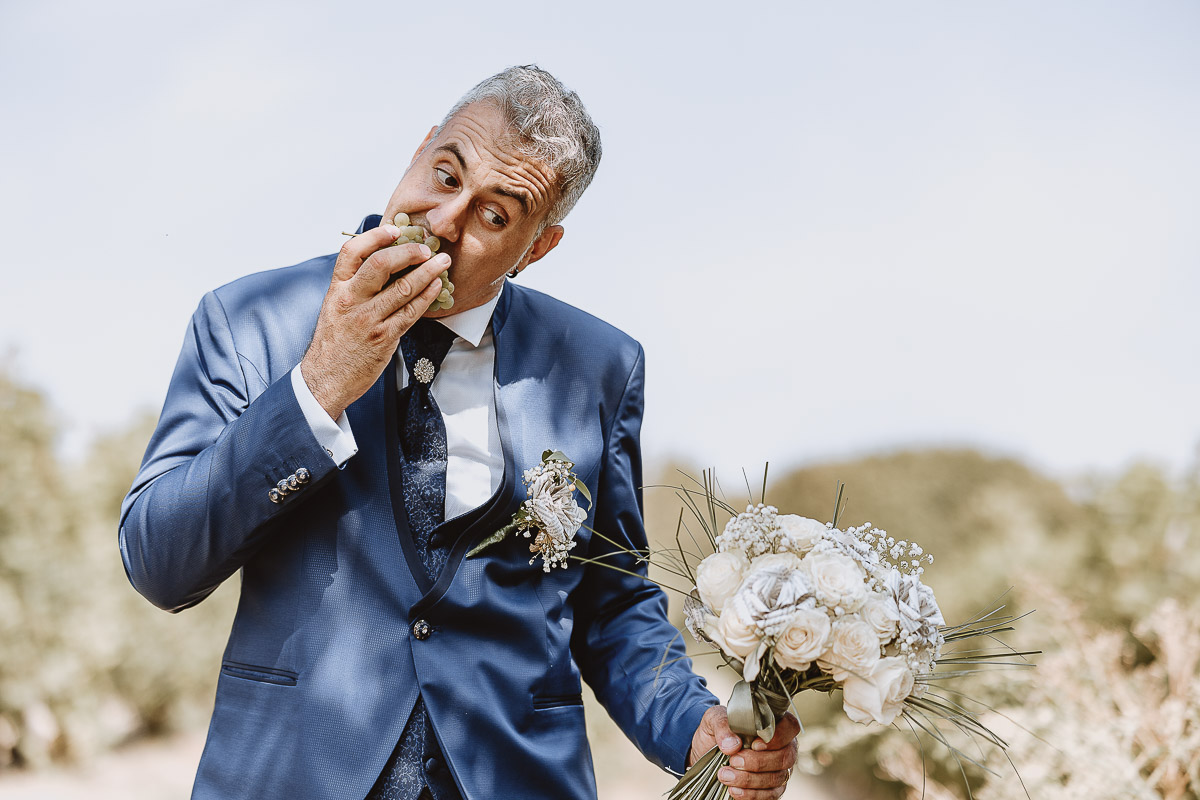 Fotografo Matrimonio in Piemonte. Ritratti di coppia degli sposi nel vigneto di famiglia a Moncucco Torinese. lo sposo mangia un grappolo d'uva.