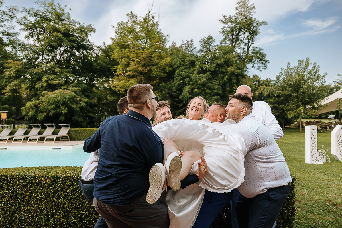 Fotografo Matrimonio in Piemonte. Ricevimento all'agriturismo Greppi di Crescentino (VC). Pranzo nuziale. Amici fanno volare la sposa che ha un'espressione tra spaventata e divertita.