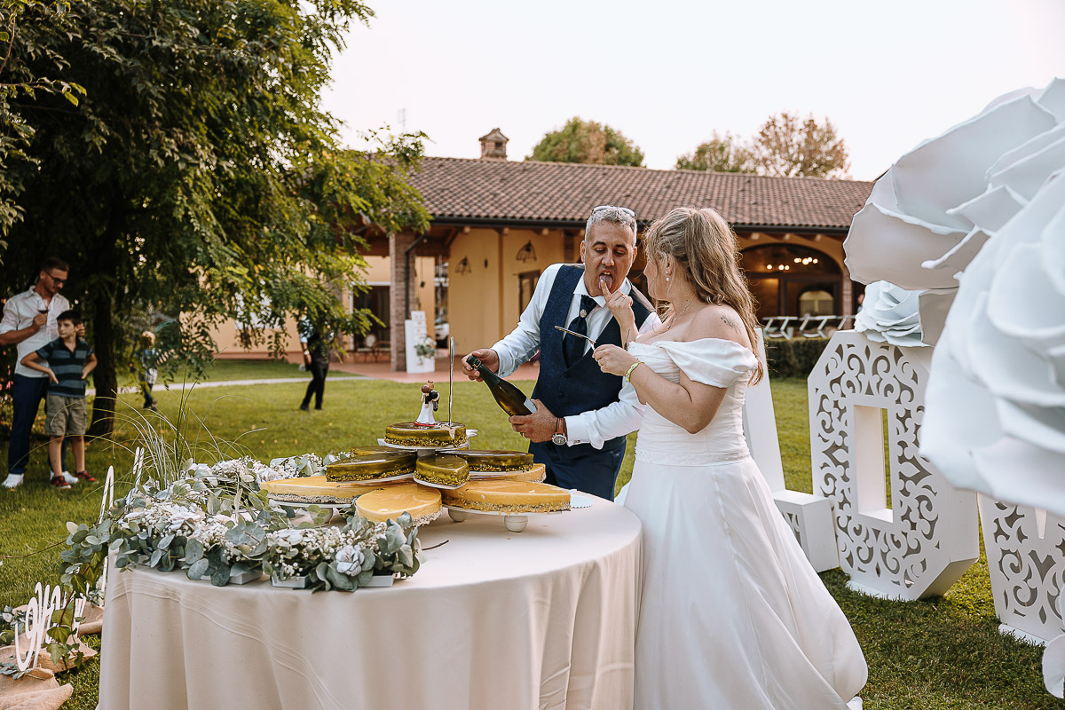 Fotografo Matrimonio in Piemonte. Ricevimento all'agriturismo Greppi di Crescentino (VC). Ricevimento. Taglio torta. Lo sposo apre la bottiglia di spumante e la sposa fa leccare un po' di torta allo sposo.