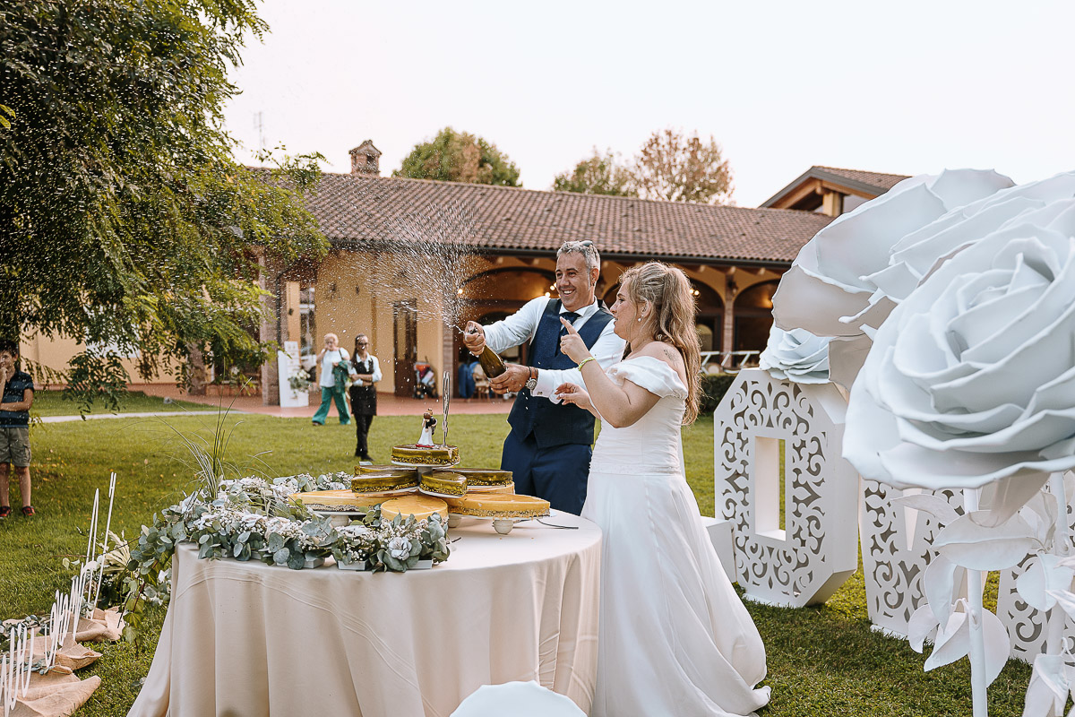 Fotografo Matrimonio in Piemonte. Ricevimento all'agriturismo Greppi di Crescentino (VC). Ricevimento. Taglio torta. Lo sposo apre la bottiglia di spumante
