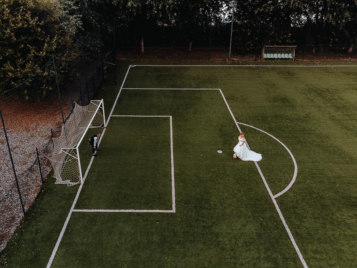 Fotografo Matrimonio in Piemonte. Ricevimento all'agriturismo Greppi di Crescentino (VC). Ricevimento. Ritratti degli sposi al campo di calcio. La sposa calcia il pallone verso la porta difesa dallo sposo. Foto aerea dal drone.