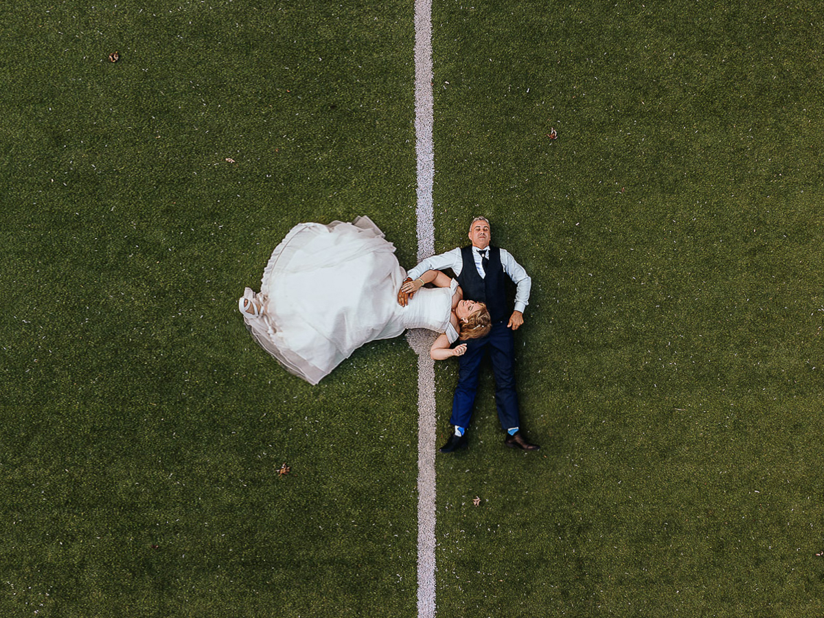 Fotografo Matrimonio in Piemonte. Ricevimento all'agriturismo Greppi di Crescentino (VC). Ricevimento. Ritratti degli sposi al campo di calcio. Sposi sdraiati sul terreno da gioco. Foto aerea dal drone.