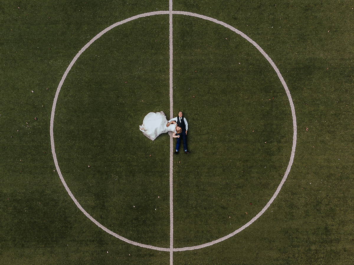 Fotografo Matrimonio in Piemonte. Ricevimento all'agriturismo Greppi di Crescentino (VC). Ricevimento. Ritratti degli sposi al campo di calcio. Sposi sdraiati sul terreno da gioco. Foto aerea dal drone. Si vede bene il cerchio di centrocampo.