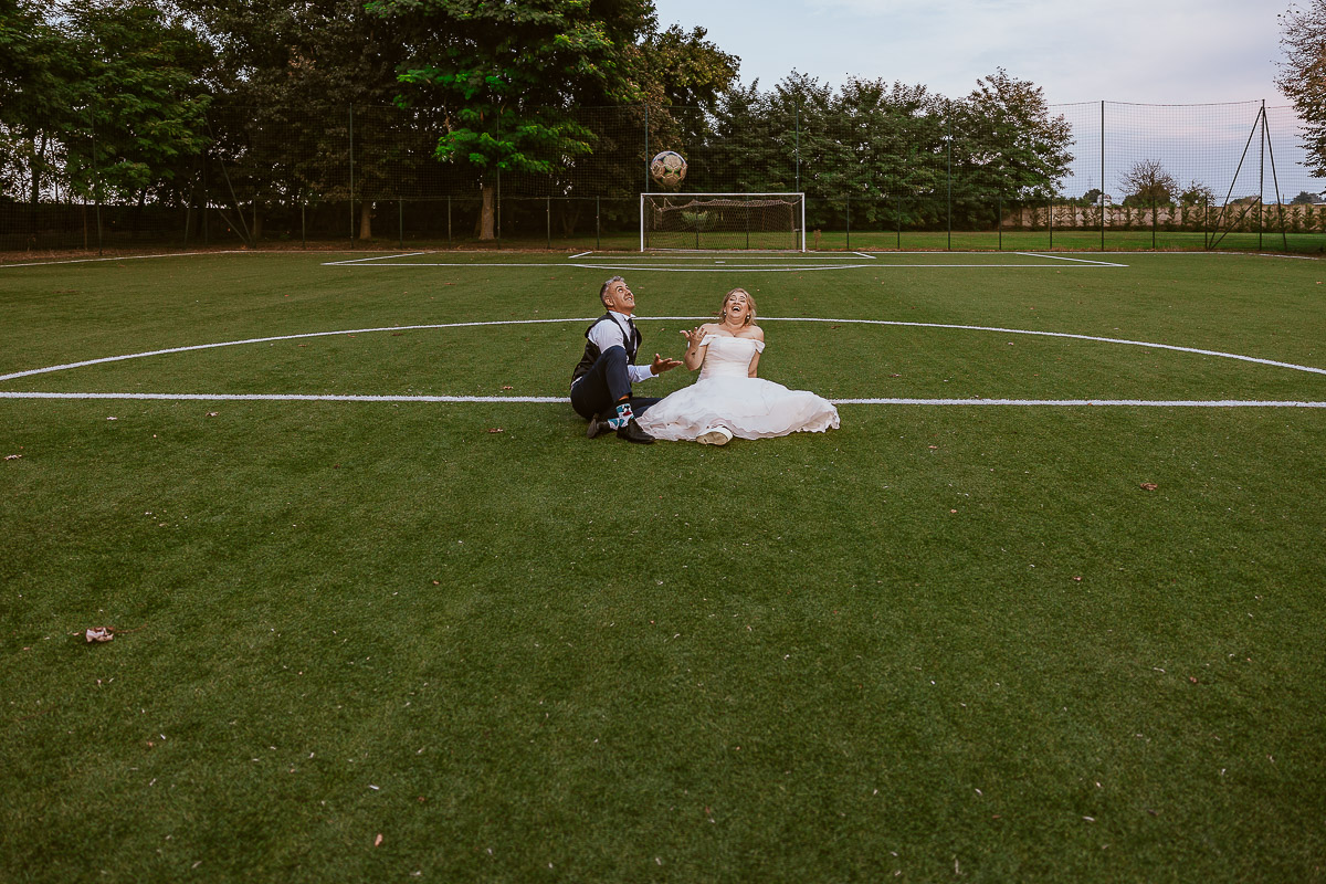 Fotografo Matrimonio in Piemonte. Ricevimento all'agriturismo Greppi di Crescentino (VC). Ricevimento. Ritratti degli sposi al campo di calcio. Sposi seduti sul terreno di gioco. lo sposo ha in mano il pallone.