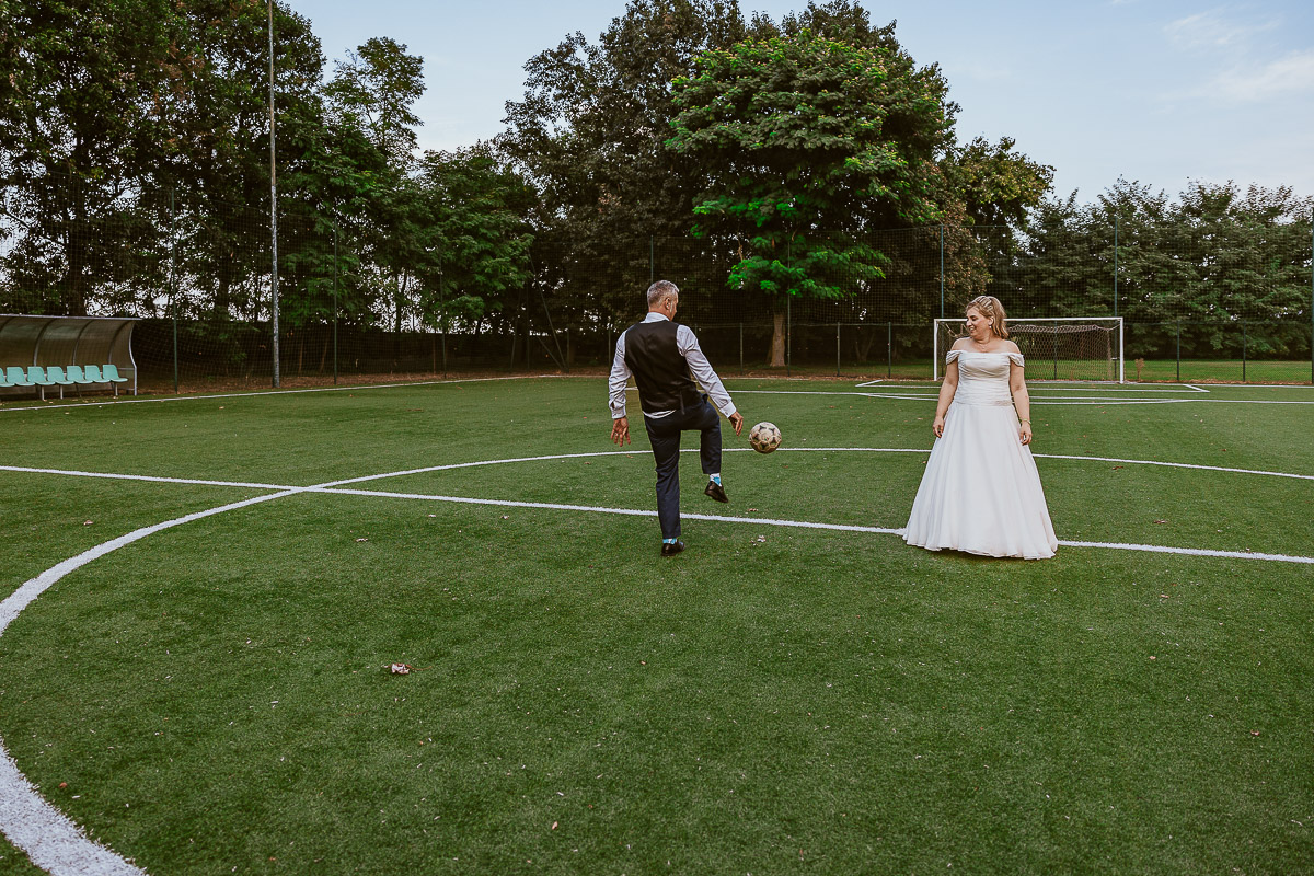 Fotografo Matrimonio in Piemonte. Ricevimento all'agriturismo Greppi di Crescentino (VC). Ricevimento. Ritratti degli sposi al campo di calcio. Sposo palleggia con il pallone. la sposa lo guarda.