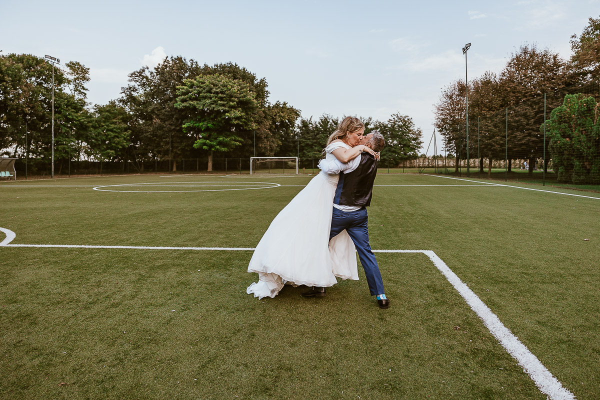 Fotografo Matrimonio in Piemonte. Ricevimento all'agriturismo Greppi di Crescentino (VC). Ricevimento. Ritratti degli sposi al campo di calcio. Lo sposo prende in braccio la sposa.