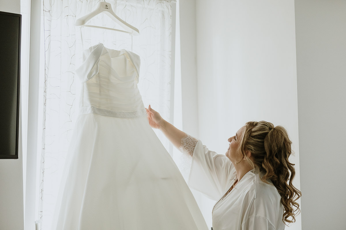 Fotografo Matrimonio in Piemonte. Preparazione a Moncucco Torinese. Sposa accarezza e guarda il suo abito.