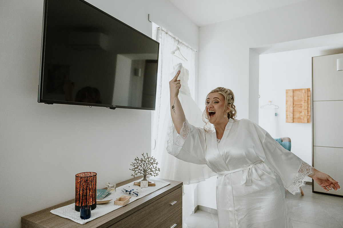 Fotografo Matrimonio in Piemonte. Preparazione a Moncucco Torinese.Sposa mostra il dito medio ai parenti per scherzo.