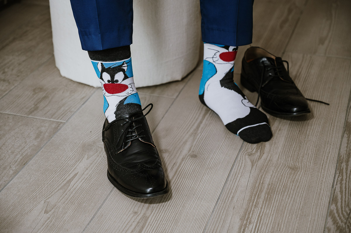 Fotografo Matrimonio in Piemonte. Preparazione a Moncucco Torinese. Sposo con le calze di Gatto silvestro si mette le scarpe.