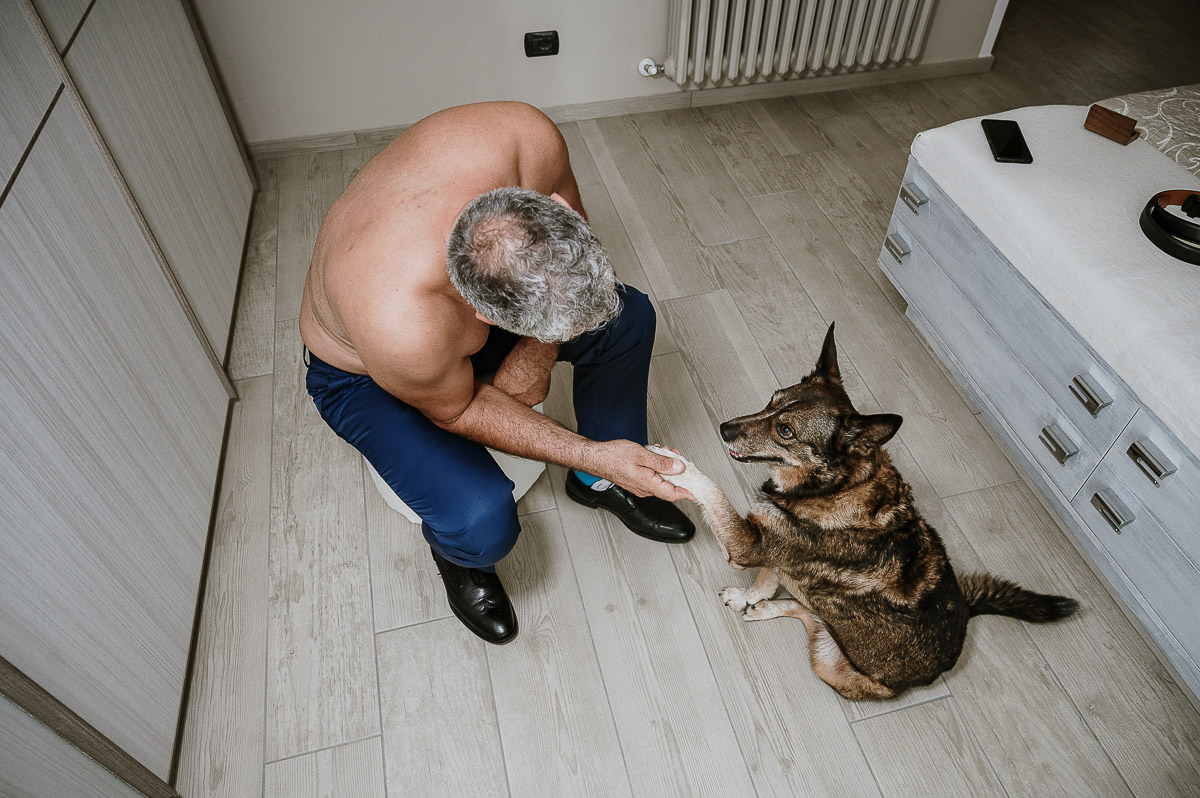 Fotografo Matrimonio in Piemonte. Preparazione a Moncucco Torinese. Sposo prende la zampa del cane.
