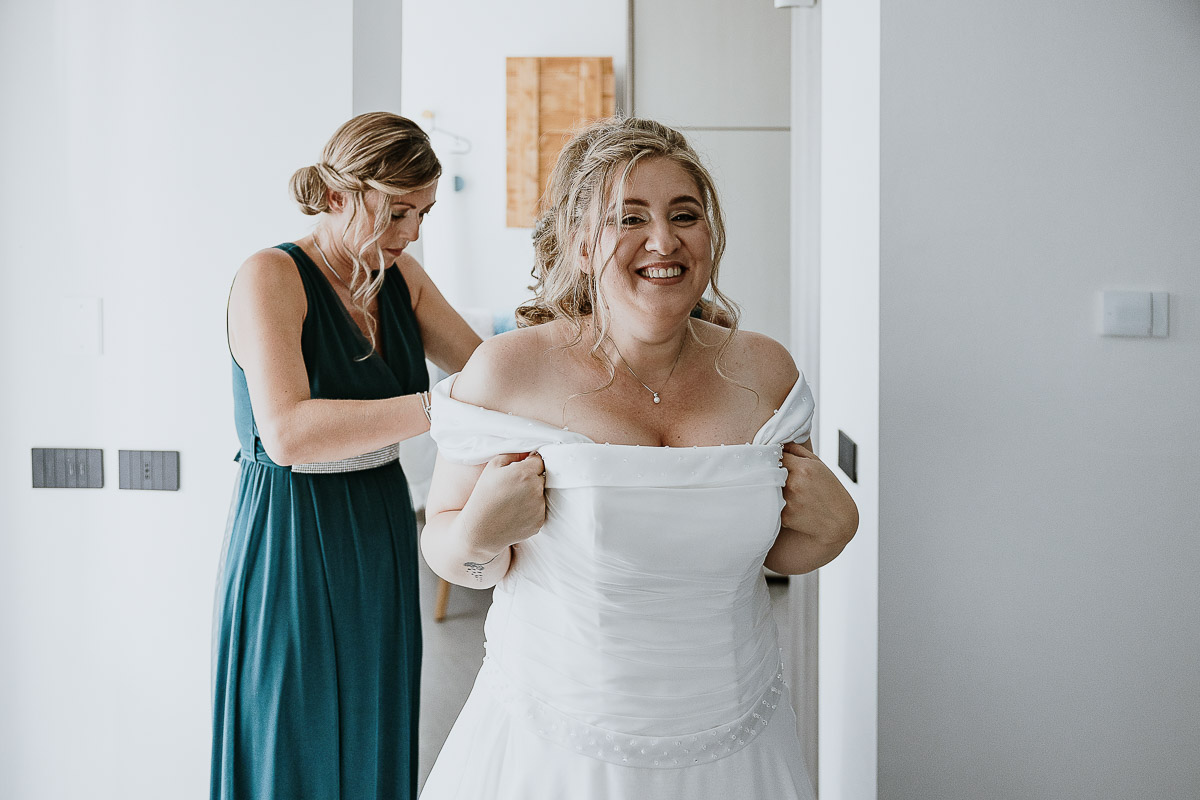Fotografo Matrimonio in Piemonte. Preparazione a Moncucco Torinese. le testimoni abbottonano il vestito della sposa.