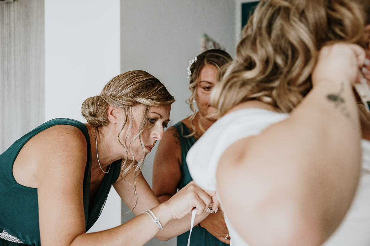 Fotografo Matrimonio in Piemonte. Preparazione a Moncucco Torinese. Le testimoni legano i nastri di chiusura del vestito della sposa.