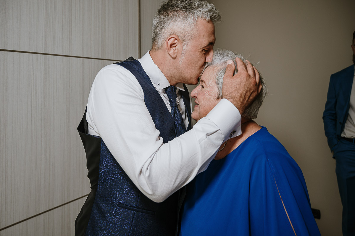 Fotografo Matrimonio in Piemonte. Preparazione a Moncucco Torinese. lo sposo bacia la mamma sulla fronte.