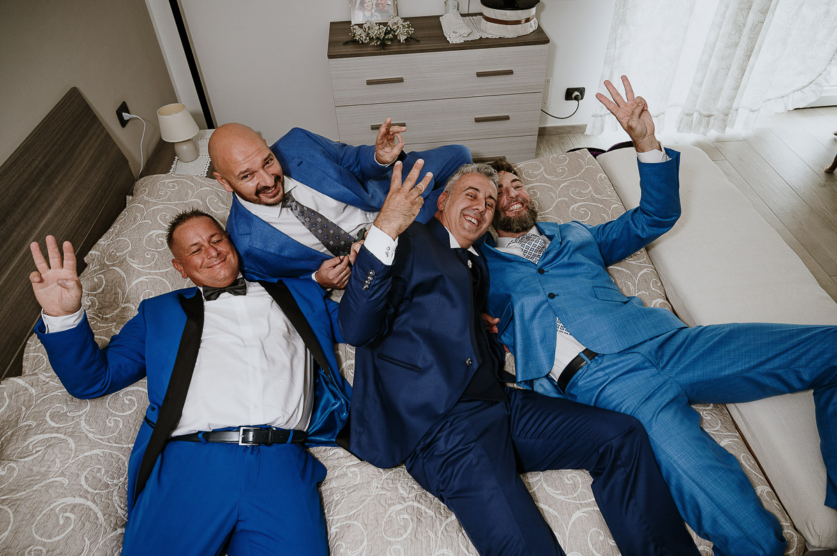 Fotografo Matrimonio in Piemonte. Preparazione a Moncucco Torinese. Sposo testimoni e un amico sdraiati sul letto
