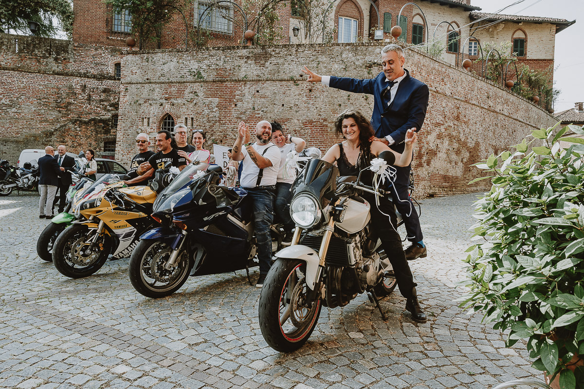 Fotografo Matrimonio in Piemonte. Cerimonia a Moriondo Torinese. Sposo sulla moto di un'amica con la parata di motociclisti.